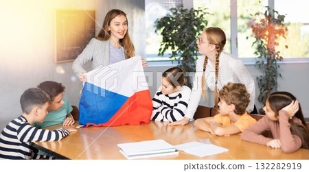 Cheerful female teacher discussing with preteens students state flag of in auditory of middle school Cheerful female teacher discussing with preteens students state flag of in auditory of middle school 132282919