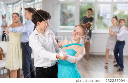 Positive teen boy and girl are dancing classic version of waltz in couple during lesson at studio Positive teen boy and girl are dancing classic version of waltz in couple during lesson at studio 132283004