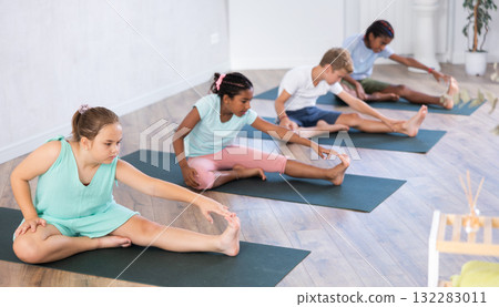 Diligent children practicing hand to toe pose of yoga on black mat in light room 132283011