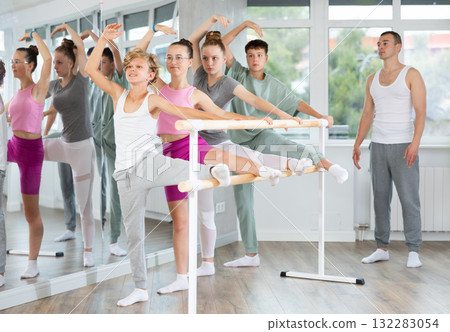 Teen ballet students prepare for classes, near ballet bare stretch legs under man teacher guidance Teen ballet students prepare for classes, near ballet bare stretch legs under man teacher guidance 132283054