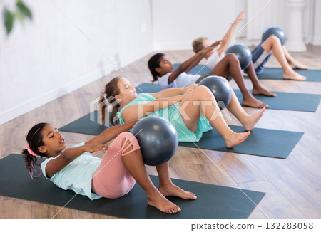 Portrait of childrens with pilates balls, pumping press during group class in fitness studio 132283058