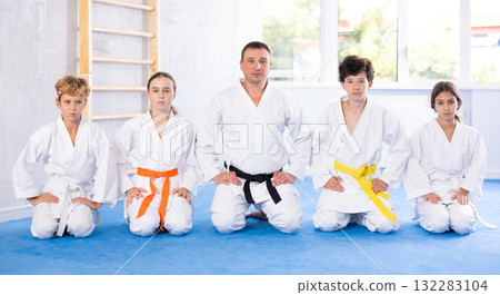 Team of young martial arts athletes is posing in gym with male coach. Team of young martial arts athletes is posing in gym with male coach. 132283104