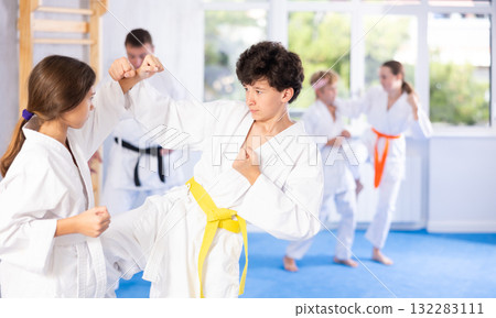 Teenagers girl and boy in kimono sparring together in gym during karate training Teenagers girl and boy in kimono sparring together in gym during karate training 132283111