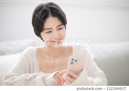 一位可愛的女士穿著白色針織衫,正看著智慧型手機。這款柔軟的米色針織衫適合春秋冬季節穿著。 一位可愛的女士穿著白色針織衫,正看著智慧型手機。這款柔軟的米色針織衫適合春秋冬季節穿著。 132284937