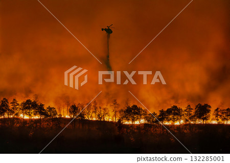 Fire fighting helicopter dropping water to put out a forest fire. Fire fighting helicopter dropping water to put out a forest fire. 132285001