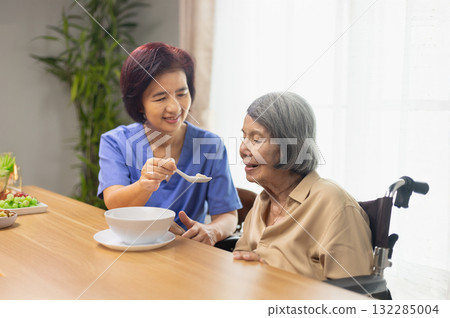 Caregiver feeding elderly asian woman with soup. Caregiver feeding elderly asian woman with soup. 132285004