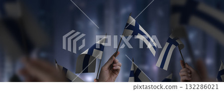 Finland flags in their hands on a blurred urban background Finland flags in their hands on a blurred urban background 132286021