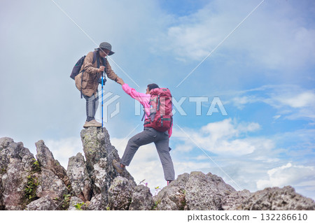 Two hikers on rocky mountain peak helping each other climb, symbol of teamwork, leadership, support, adventure, success, trust, exploration and outdoor lifestyle motivation in nature. 132286610