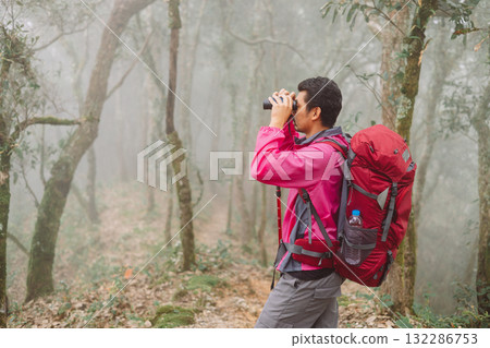 Traveler with backpack using binoculars in foggy forest, symbol of adventure, exploration, discovery, outdoor lifestyle, hiking journey, curiosity and inspiration for travel in nature. 132286753