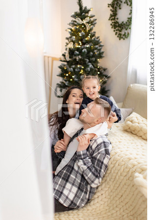 A happy family poses together in front of a Christmas tree, creating a warm and festive holiday scene. 132286945