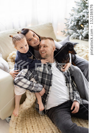 A happy family poses together with their pet dachshund in a cozy indoor setting, creating a warm and loving atmosphere. A happy family poses together with their pet dachshund in a cozy indoor setting, creating a warm and loving atmosphere. 132286976