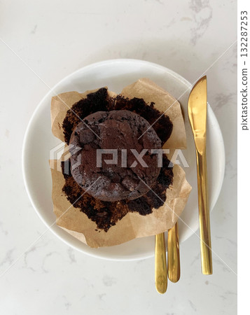 Close-up of a delicious chocolate lava muffin on parchment paper over white plate, isolated on light background with copy space, perfect dessert photo for bakery menu or food advertising design 132287253