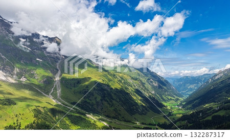 Majestic Alpine Valley Vista Lush Greenery, Towering Mountains, and Dramatic Cloudscape 132287317