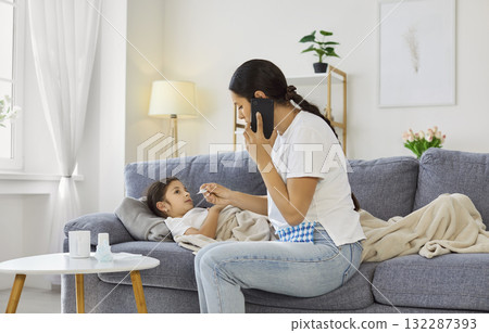 Mother checking temperature of child while calling doctor for consultation Mother checking temperature of child while calling doctor for consultation 132287393