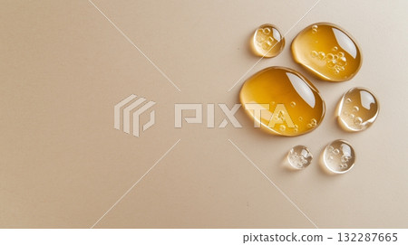Honey-colored liquid droplets on beige surface with bubbles highlighting fluid texture 132287665