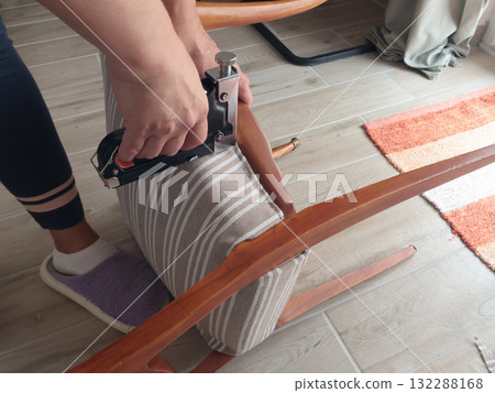 Anonymous person restore old vintage chair in home. Fabric replacement. Antique furniture and modern striped linen and cotton fabric. Hobbies, crafts, and retro-minimalist style. 132288168