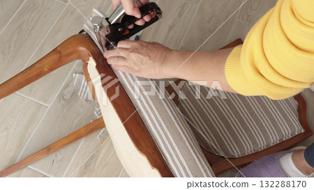 Anonymous person restore old vintage chair in home. Fabric replacement. Antique furniture and modern striped linen and cotton fabric. Hobbies, crafts, and retro-minimalist style. Anonymous person restore old vintage chair in home. Fabric replacement. Antique furniture and modern striped linen and cotton fabric. Hobbies, crafts, and retro-minimalist style. 132288170