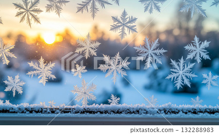 A macro photograph of intricate frost snowflakes on a window pane with a beautiful, warm winter sunrise and snowy landscape blurred in the background. A macro photograph of intricate frost snowflakes on a window pane with a beautiful, warm winter sunrise and snowy landscape blurred in the background. 132288983