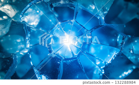A macro view of shattered blue ice with a bright light shining through the geometric cracks, creating a dynamic and abstract winter background. 132288984