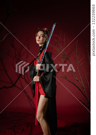 Woman poses in traditional Japanese dress with a sword in a studio setting 132289668