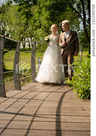 Couple walks hand in hand over bridge in sunny outdoor wedding celebration 132289708