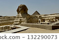 An ancient statue seen from the front and a small pyramid in the background - an adventurous desert tourist scene 132290073
