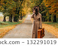 European woman in coat and hat walks along  yellow autumn trees 132291019