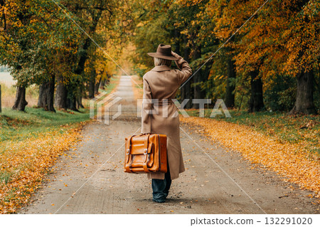 European woman in coat and hat walks along  yellow autumn trees 132291020