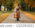 European woman in coat and hat walks along  yellow autumn trees 132291021