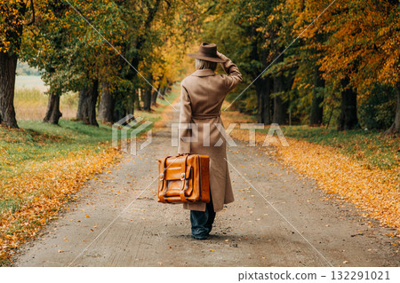 European woman in coat and hat walks along  yellow autumn trees 132291021