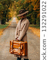 European woman in coat and hat walks along  yellow autumn trees 132291022