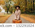 European woman in coat and hat walks along  yellow autumn trees 132291024
