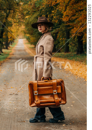 European woman in coat and hat walks along  yellow autumn trees 132291025