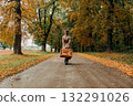 European woman in coat and hat walks along  yellow autumn trees 132291026