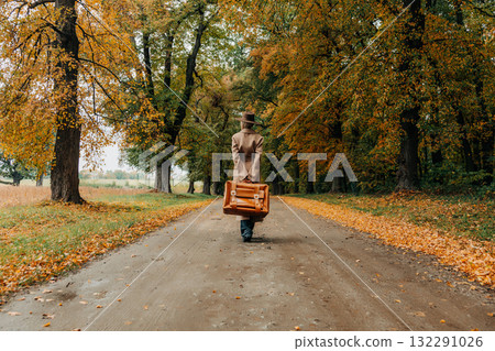 European woman in coat and hat walks along  yellow autumn trees 132291026
