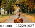 European woman in coat and hat walks along  yellow autumn trees 132291027