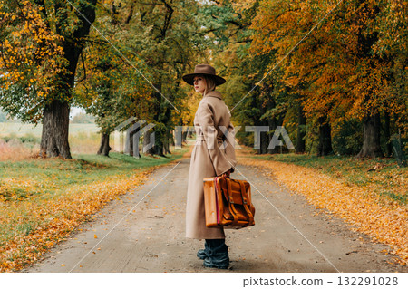 European woman in coat and hat walks along yellow autumn trees European woman in coat and hat walks along yellow autumn trees 132291028