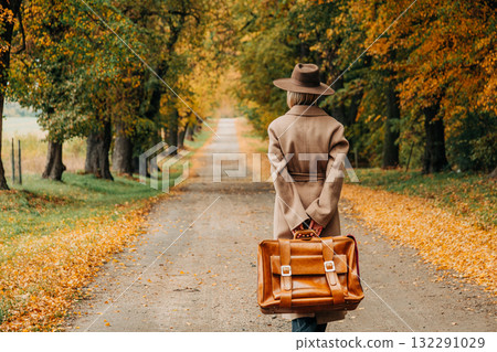 European woman in coat and hat walks along yellow autumn trees European woman in coat and hat walks along yellow autumn trees 132291029