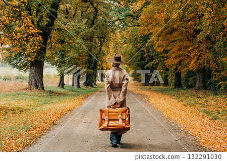 European woman in coat and hat walks along  yellow autumn trees 132291030