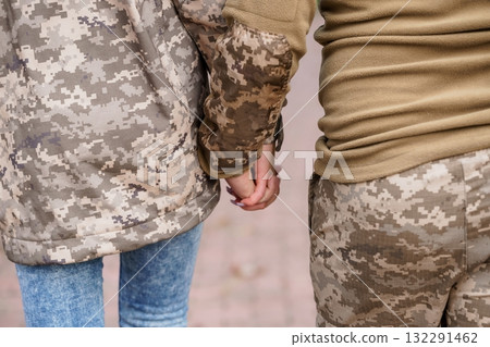Two People Holding Hands in Military Camouflage Clothing, Close-Up, Brown and Green Tones, Tactical Gear, Relationship Concept, Support, Unity. 132291462