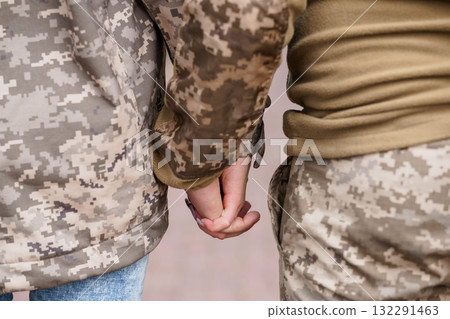 Two Soldiers Holding Hands in Uniform, Camouflage Pattern, Close-Up, Connection, Love, Military Romance, Warm Tones, Textured Fabric, Relationship. 132291463