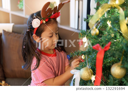 Festive Spirit. Young girl decorating Christmas tree with ornaments. Festive Spirit. Young girl decorating Christmas tree with ornaments. 132291694