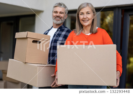 Happy senior couple moving boxes outside residential entrance Happy senior couple moving boxes outside residential entrance 132293448