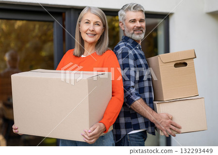 Mature couple holding moving boxes smiling at front door of house Mature couple holding moving boxes smiling at front door of house 132293449