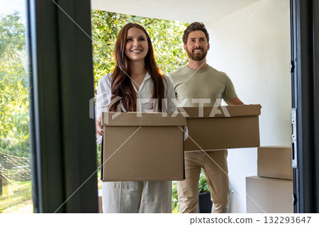 Young man and woman with cardboard boxes in hands entering the house Young man and woman with cardboard boxes in hands entering the house 132293647