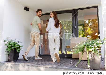 Happy couple looking excited while carrying cardboard boxes into the new house Happy couple looking excited while carrying cardboard boxes into the new house 132293685