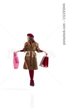 Confident woman in brown coat jumping with shopping bags in expressive balance pose 132293844