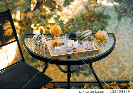 Outdoor glass table scene with colorful gourds and a tray of vitamins and supplements, surrounded by fall foliage and chair. Preventive wellness in everyday life, proactive health, lifestyle medicine 132293859