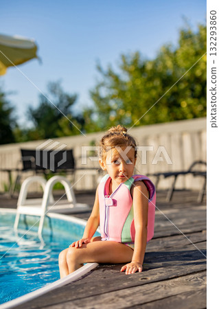 Cute kid in life jacket sitting on the swimming pool edge 132293860