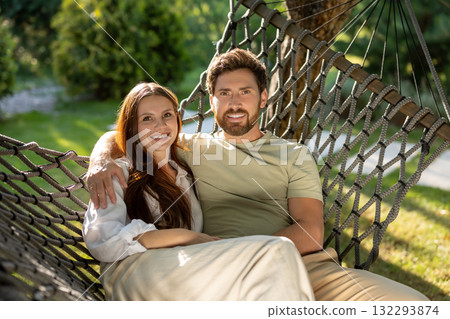 Cute smiling couple enjoying time together while sitting in hammock in the park Cute smiling couple enjoying time together while sitting in hammock in the park 132293874